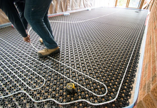 Photographie en gros plan d'un carreleur professionnel en équipement de travail (gilet de sécurité, bottes) appliquant du carrelage sur un mur ou un sol intérieur. L'artisan doit tenir un outil de pose de carrelage (spatule crantée, niveau, truelle) et on doit voir les carreaux partiellement posés sur la surface avec du mortier-colle. L'arrière-plan doit montrer un environnement de chantier ou une zone rénovée avec les matériaux visibles. La composition doit mettre en évidence le professionnalisme, la précision de la pose et le travail de finition du carrelage, distinctement différente d'une scène de chape liquide.
